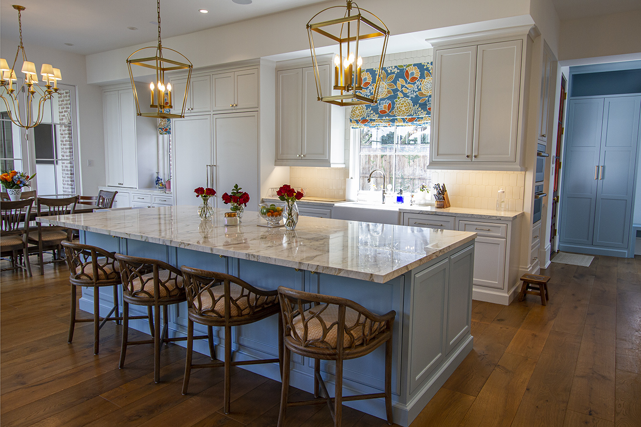 Open-plan kitchen with a large marble island, woven counter stools, brass pendants and pale cabinetry