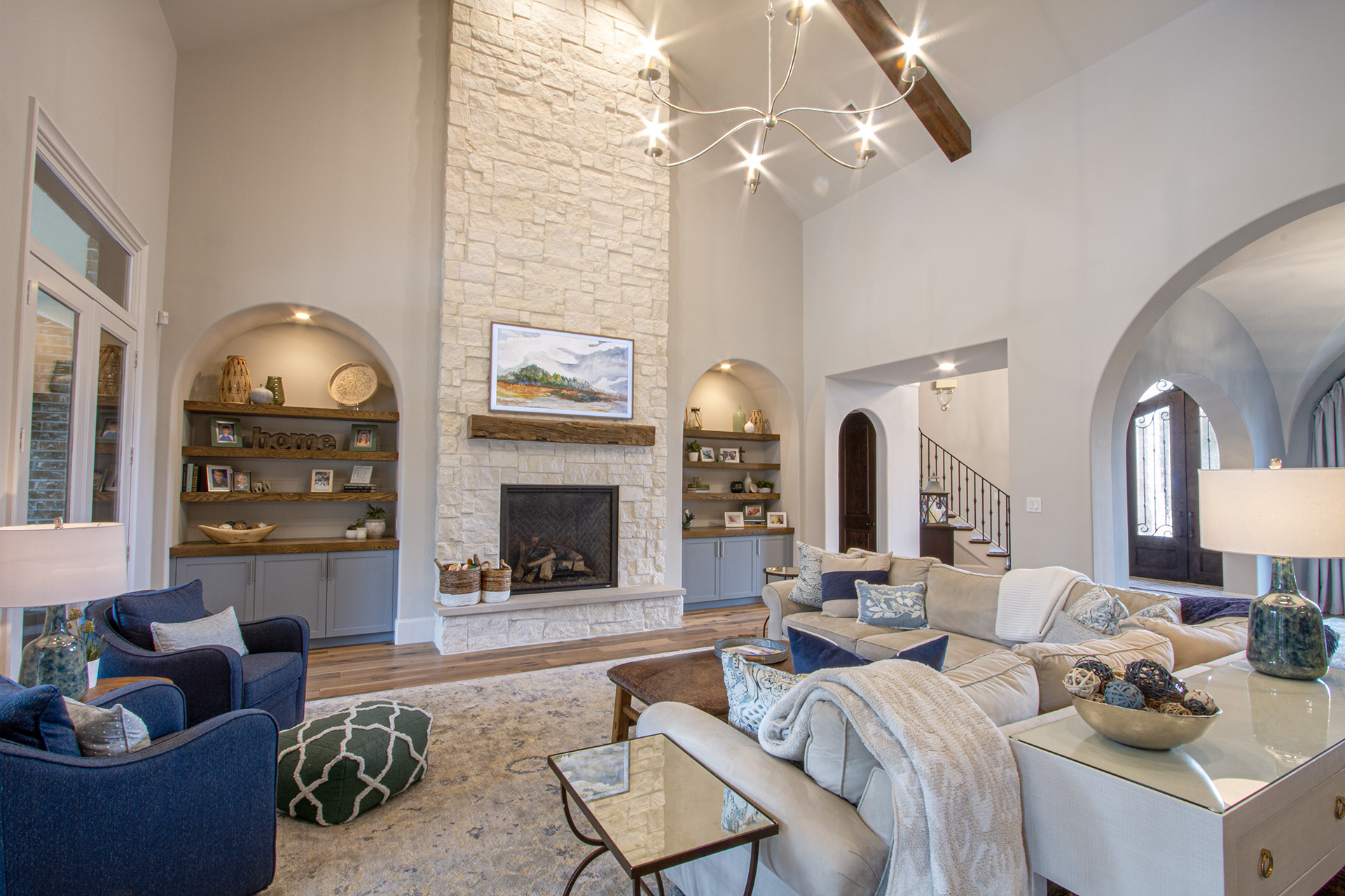Double-height living room with a stone fireplace, arched openings, blue armchairs and a starburst chandelier