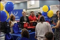 A group gathered around the backpack table under blue and yellow balloons
