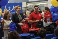 Volunteers and families exchanging backpacks across the branded table