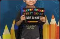 A child holding a 'First Day of Kindergarten' sign against a coloured pencil backdrop