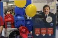 Backpacks stacked on the table beside a firm-branded display board and balloons