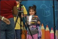 A young girl holding a first-day sign, photographed against the coloured pencil backdrop