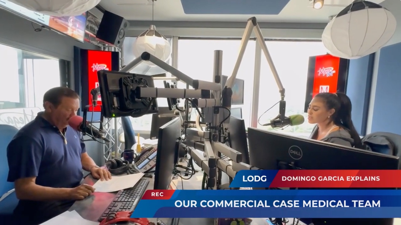 Still from a firm explainer video: two people talking at a desk under a lower-third reading 'Our commercial case medical team'